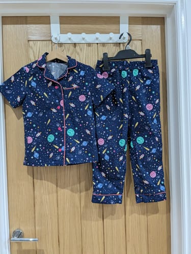 Customer's pajama set made from Outer Space Cotton Poplin Fabric, featuring a colorful space print and pink piping, hanging on a door.