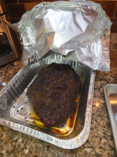 Customer's cooked USDA Prime Brisket with a dark crust, resting in its juices in a foil pan.