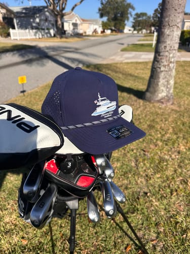 Reviewer's navy hat with custom boat artwork resting on a golf bag outdoors.