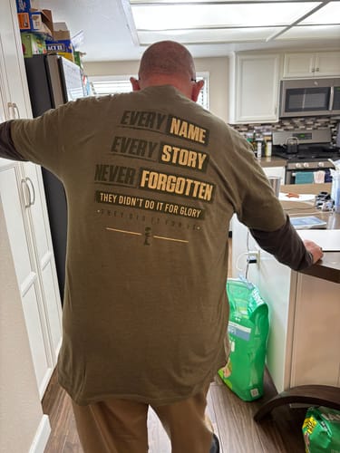 Reviewer showing the back of the green T.V.P. Elite Membership t-shirt with memorial text.