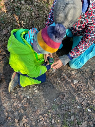 Ein Kunde zeigt Kinder, die draußen mit dem grünen Abenteuer-Mikroskop den Boden untersuchen.