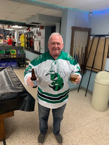 Customer smiling in a white and green personalized hockey jersey with a large hornet graphic on the front.