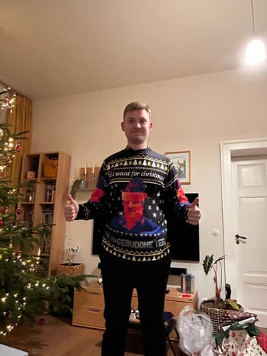 Kunde trägt den HAGEBUDDNE TEE - Christmas Ugly Sweater und gibt in einem Wohnzimmer zwei Daumen hoch.