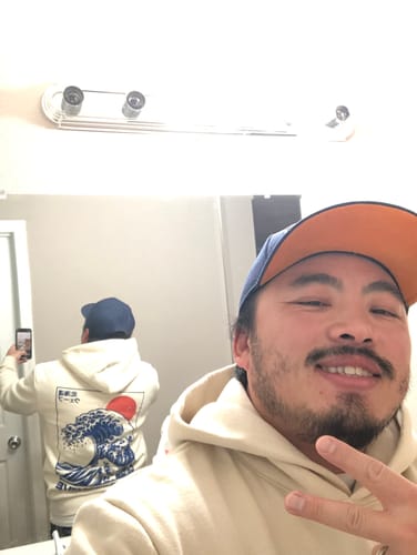 Reviewer taking a mirror selfie to show the fit and back graphic of their cream GREATWAVE HOODIE.