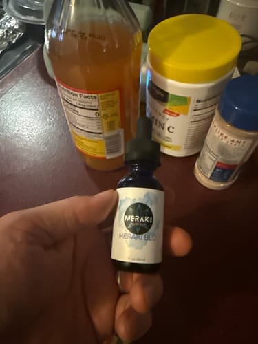 Reviewer's hand holding a small bottle of Meraki Blu Methylene Blue on a kitchen counter.