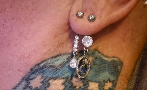 Reviewer wearing the Purple Rain Belly Dangle as a shiny earring in their ear.