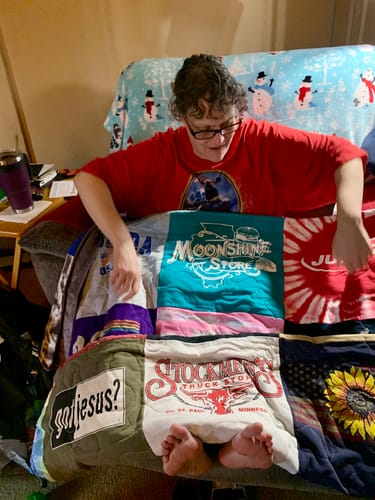 Reviewer sitting on a couch, looking down at their colorful Fuzz Monsta® T-Shirt Quilt made from memorable t-shirts.