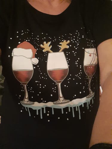 Eine Kundin trägt das schwarze „Weihnachtswein“-Shirt, das drei Weingläser mit weihnachtlichen Motiven wie einer Weihnachtsmütze zeigt.