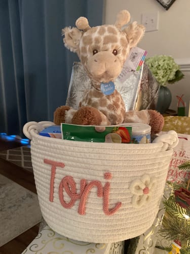 Reviewer's personalized white knitted basket with 'Tori' in pink yarn and a flower, holding a plush giraffe and other gifts.