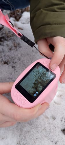 Ein Kunde hält das rosa Abenteuer-Mikroskop in der Hand, dessen Bildschirm eine vergrößerte Ansicht von Schnee zeigt.