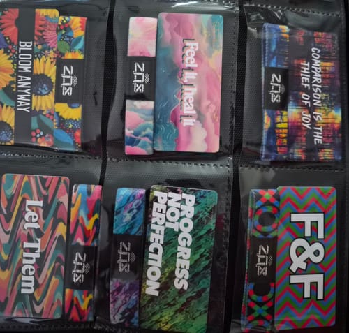 Reviewer's colorful bracelets from the Self-Care Pack, including 'Progress Not Perfection,' arranged in a collector's folder.