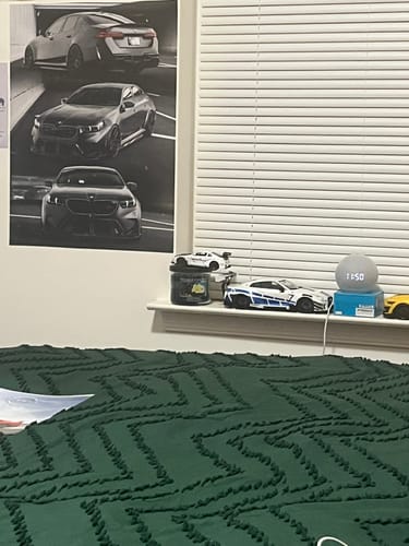 Reviewer's black and white TCG89 TRIPLE poster showing three cars, hanging on a bedroom wall.