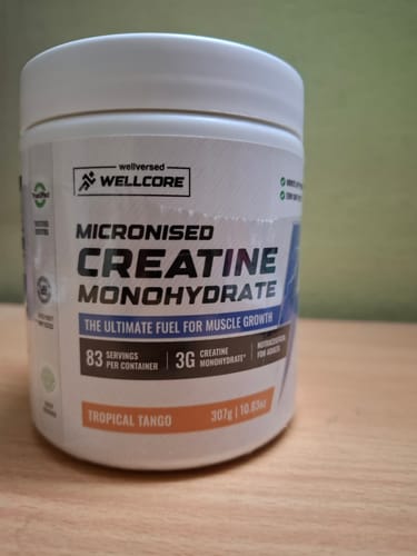 Customer's white tub of Wellcore Micronised Creatine Monohydrate in Tropical Tango flavor, sitting on a wooden surface.