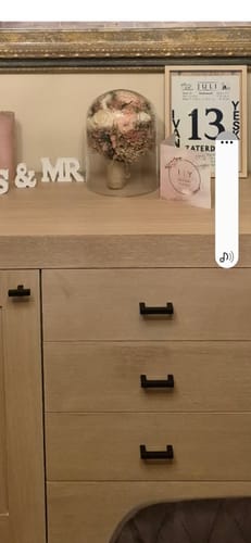 Recensent toont de glazen decoratie stolp, waarin een boeket bloemen staat, op een houten dressoir.