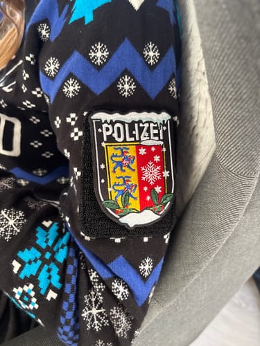 Rezensent zeigt den Polizei Xmas Textil-Länderpatch am Ärmel eines gemusterten Pullovers.