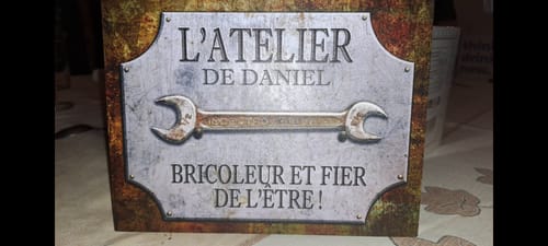 Gros plan sur la pancarte personnalisée du client, de style métal, indiquant 'L'ATELIER DE DANIEL'.