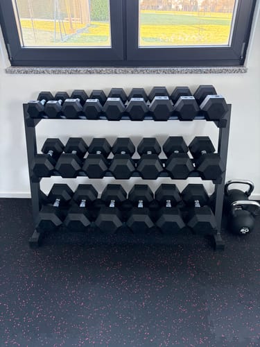 Kunde zeigt das Hexagon Hantel Set, ordentlich aufgereiht auf einem schwarzen, dreistufigen Hantelständer.