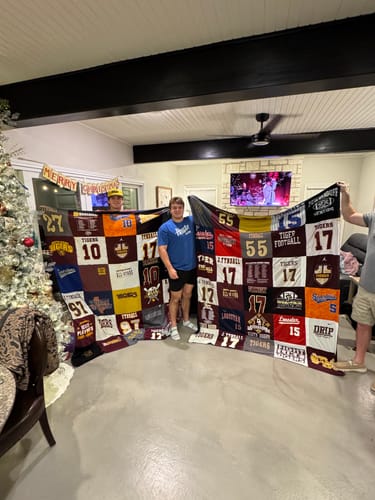 Customers holding two large Premium T Shirt Quilts made from sports jerseys in a living room.