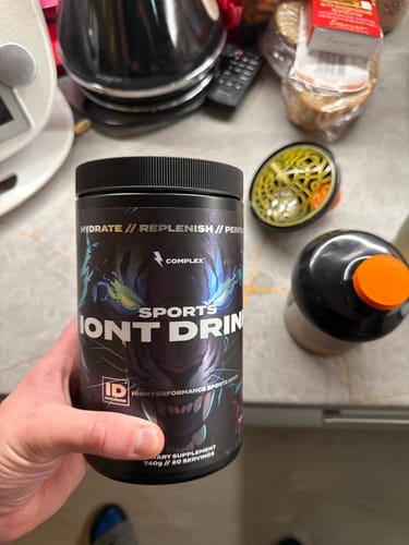 Reviewer holding a black tub of Complex Iont Drink in their hand, with a kitchen counter in the background.
