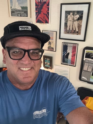 Customer smiling while wearing the black Big Camp Hat with contrast stitching in a room with framed pictures.