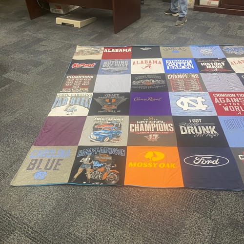 Customer's large Premium T Shirt Quilt, made from many colorful shirts, spread out on a carpeted office floor.