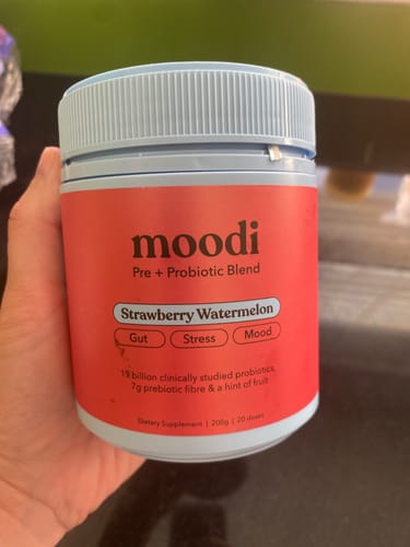Customer holding the Moodi Pre + Probiotic Blend tub in the Strawberry Watermelon flavor.