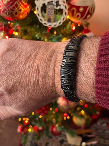 Customer wearing the personalized black bracelet on their wrist, with a festive Christmas tree in the background.