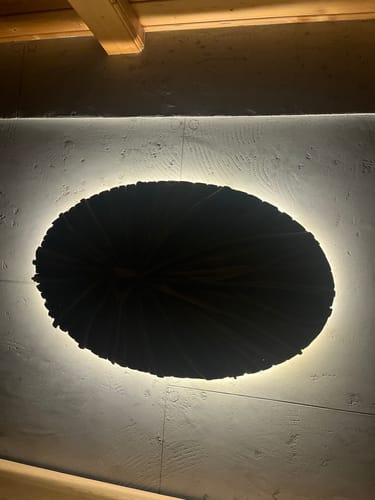 Die Wandlampe Holz LUNAR eines Kunden ist eingeschaltet und erzeugt eine warme, indirekte Beleuchtung an der Wand.