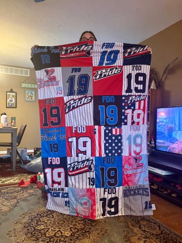 Reviewer holds up a large Premium T Shirt Quilt made from their daughter's colorful softball jerseys.