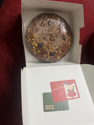 Reviewer's Christmas Plum Cake, studded with fruit and nuts, seen wrapped inside its white box.