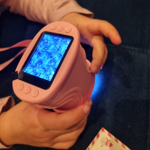 Ein Kind hält das rosa Edubini Abenteuer-Mikroskop. Der Bildschirm zeigt eine leuchtende blaue vergrößerte Struktur.