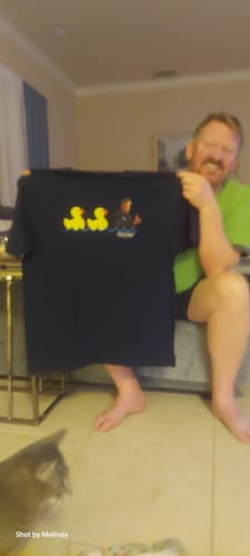 Customer smiling while holding up the dark Duck Duck Goose Top Gun Shirt he received as a gift.