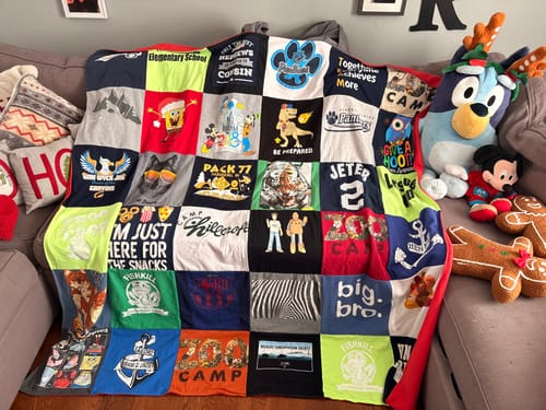 A customer's colorful Premium T-Shirt Quilt, made from various shirts, displayed on a couch.