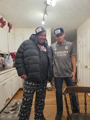 A reviewer and another person standing in a kitchen, both wearing the black Georgia Plate Hat.