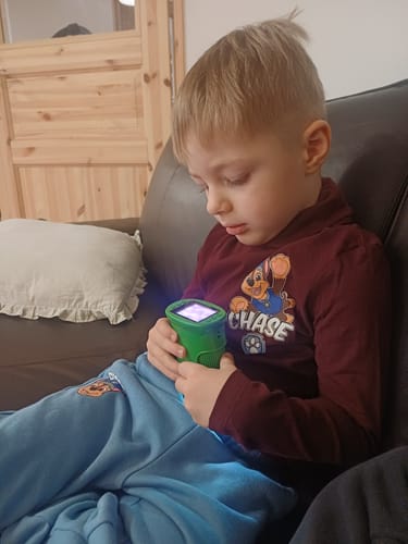 Ein Kind schaut auf einem Sofa sitzend konzentriert auf das beleuchtete Display des grünen Edubini Abenteuer-Mikroskops.