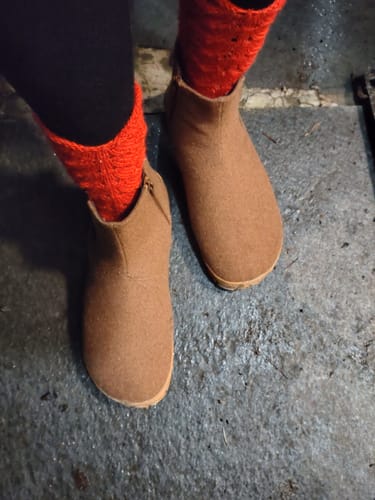 Arvostelijan jalassa ruskeat Vaistoa Sulo -paljasjalkanilkkurit ja punaiset sukat ulkona.