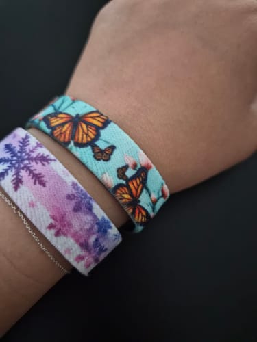 Reviewer's wrist wearing the light blue Butterfly Kisses Bracelet, featuring an orange butterfly design, next to another bracelet.