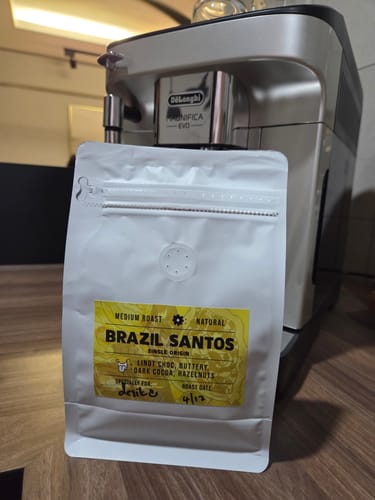Reviewer's white pouch of Brazil Santos coffee beans resting in front of a silver espresso machine.