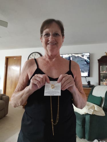 Reviewer smiling while holding up the Forever Love Necklace, which is still attached to its message card.
