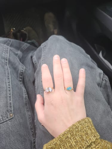 Reviewer's hand showing two rings, including a gold Pia Birthstone Ring with a light blue stone on the index finger.