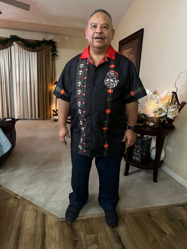 A customer stands in a living room wearing the black El Sancho Clause Guayabera with a red collar.
