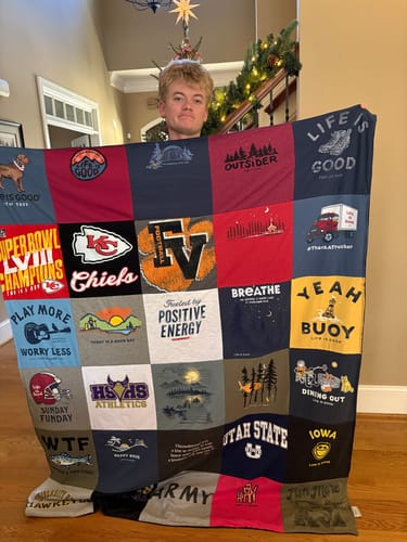 A person holds up their finished Premium T Shirt Quilt, showcasing the colorful patchwork of different shirts.