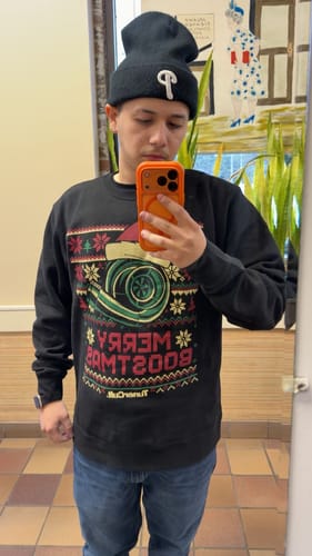 Reviewer taking a mirror selfie while wearing the black MERRY BOOSTMAS CHRISTMAS SWEATER.
