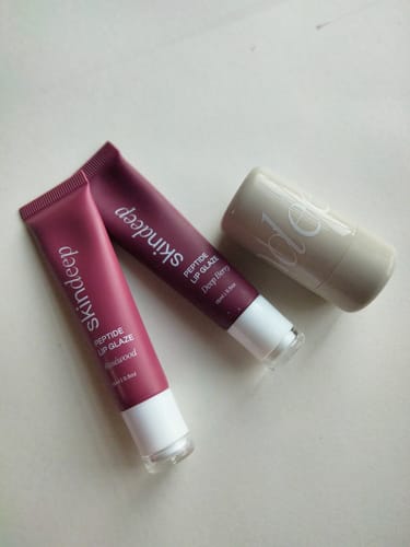 Reviewer's two Peptide Lip Glaze tubes in Rosewood and Deep Berry, pictured next to a blush stick.