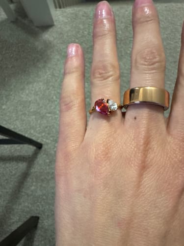 Customer's hand wearing the Leesha Birthstone Ring with two pear-cut stones, one red and one white, next to a plain gold band.