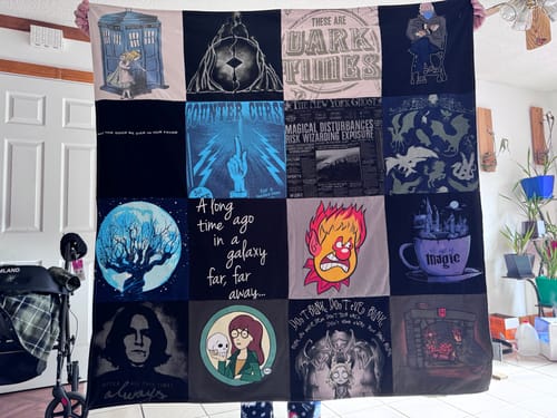 Reviewer holding up a large Premium T Shirt Quilt featuring various pop culture t-shirts in a grid layout.