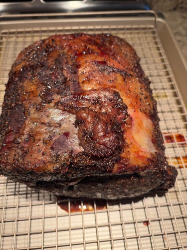 Customer's smoked prime rib with a dark, seasoned crust resting on a wire cooling rack after cooking.