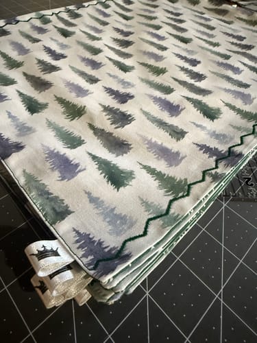 Customer's folded Watercolor Fir Trees Fabric on a cutting mat, showing the tree print and a green zig-zag stitch on the edge.