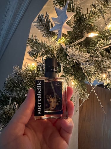 Customer's hand holding a bottle of Fractal Witch perfume in front of a decorated Christmas tree.