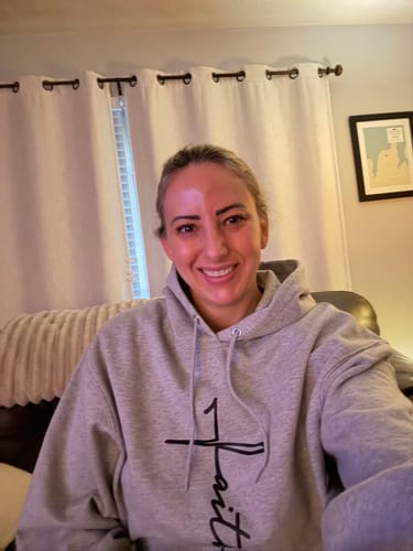 Reviewer smiling while wearing a comfortable grey hoodie with a black "Faith" cross graphic on the front.